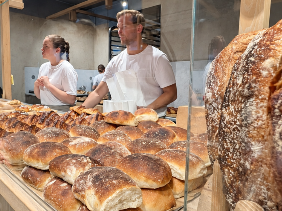 Bakers behind the glass counter at Lillebrors Bageri, with breads and a large sourdough loaf in front